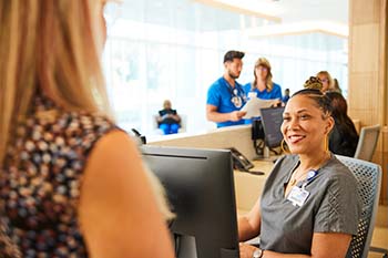 Photo of a woman checking in with another woman at a desk.