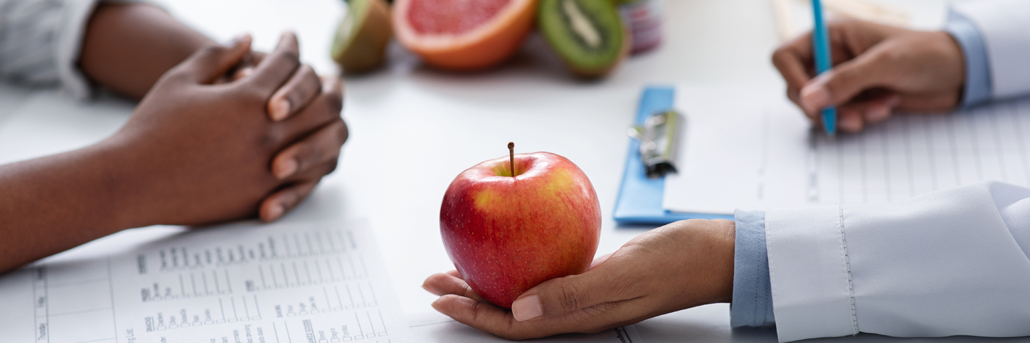 Doctor holding an apple while writing on a sheet of paper.